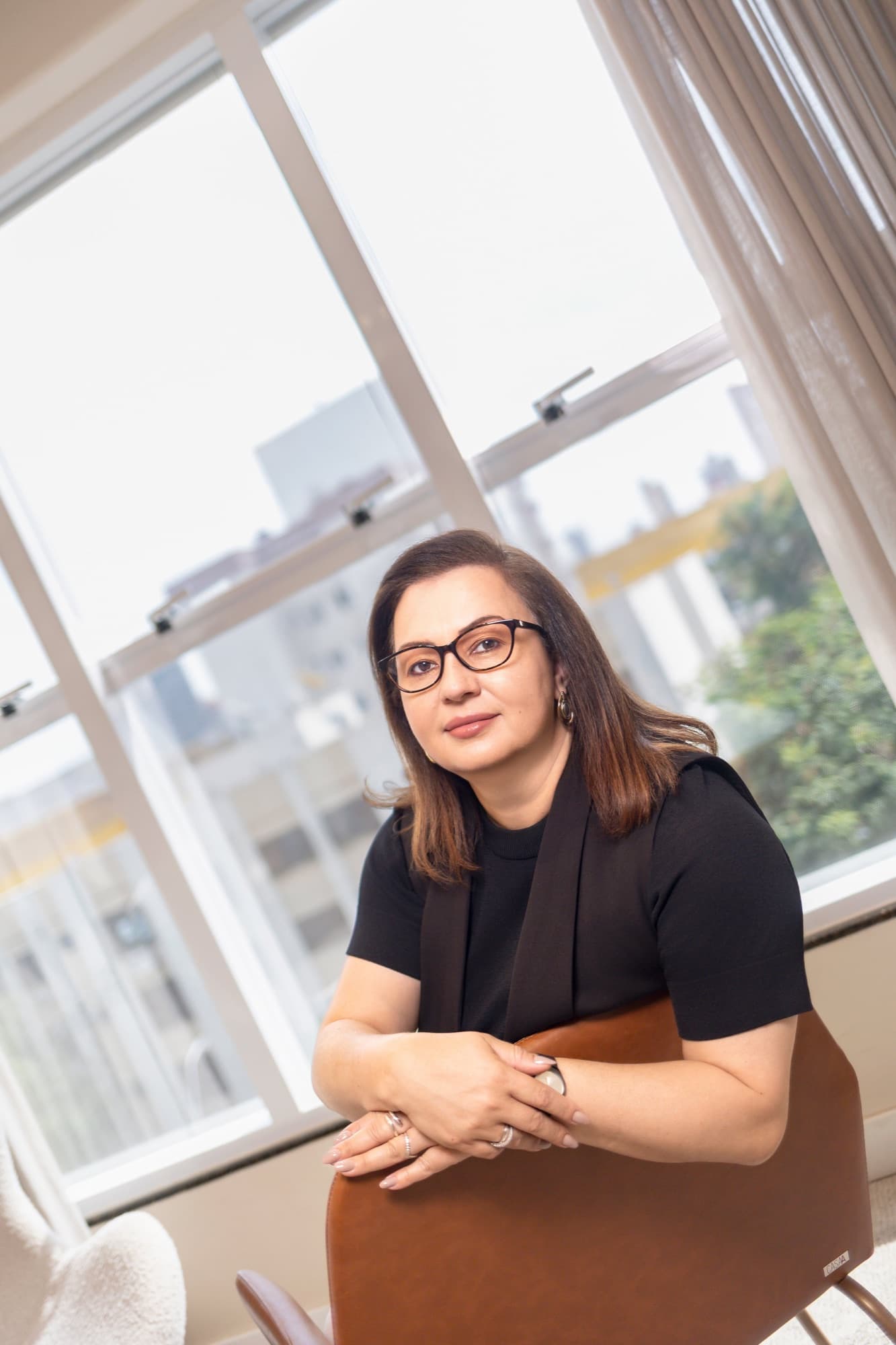 Simone Miranda, representante comercial, sentada em escritório com vista para a cidade